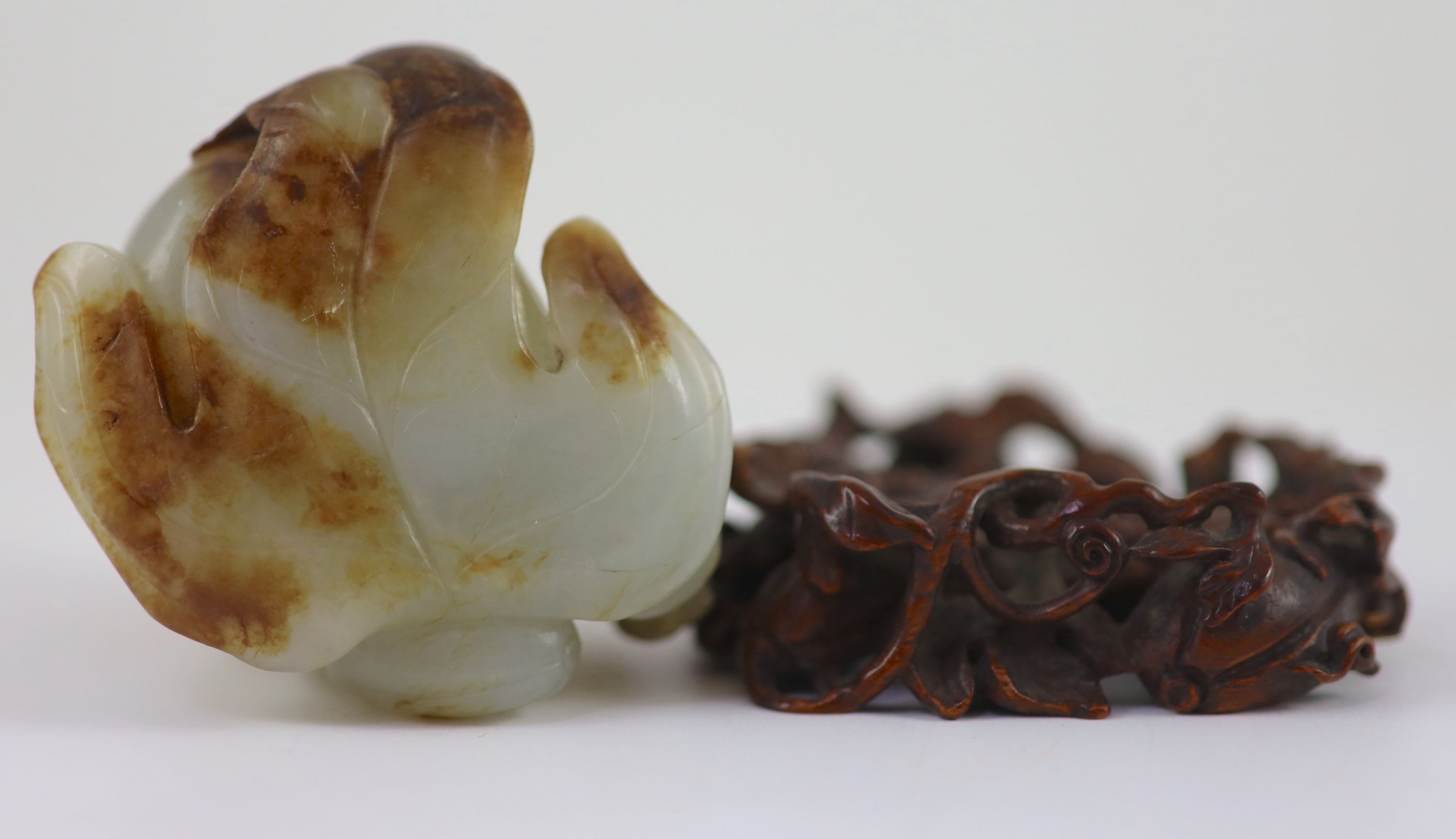 A Chinese pale celadon and russet jade 'boy' jar and cover, 8.3 cm high, the hardwood stand carved as a vine